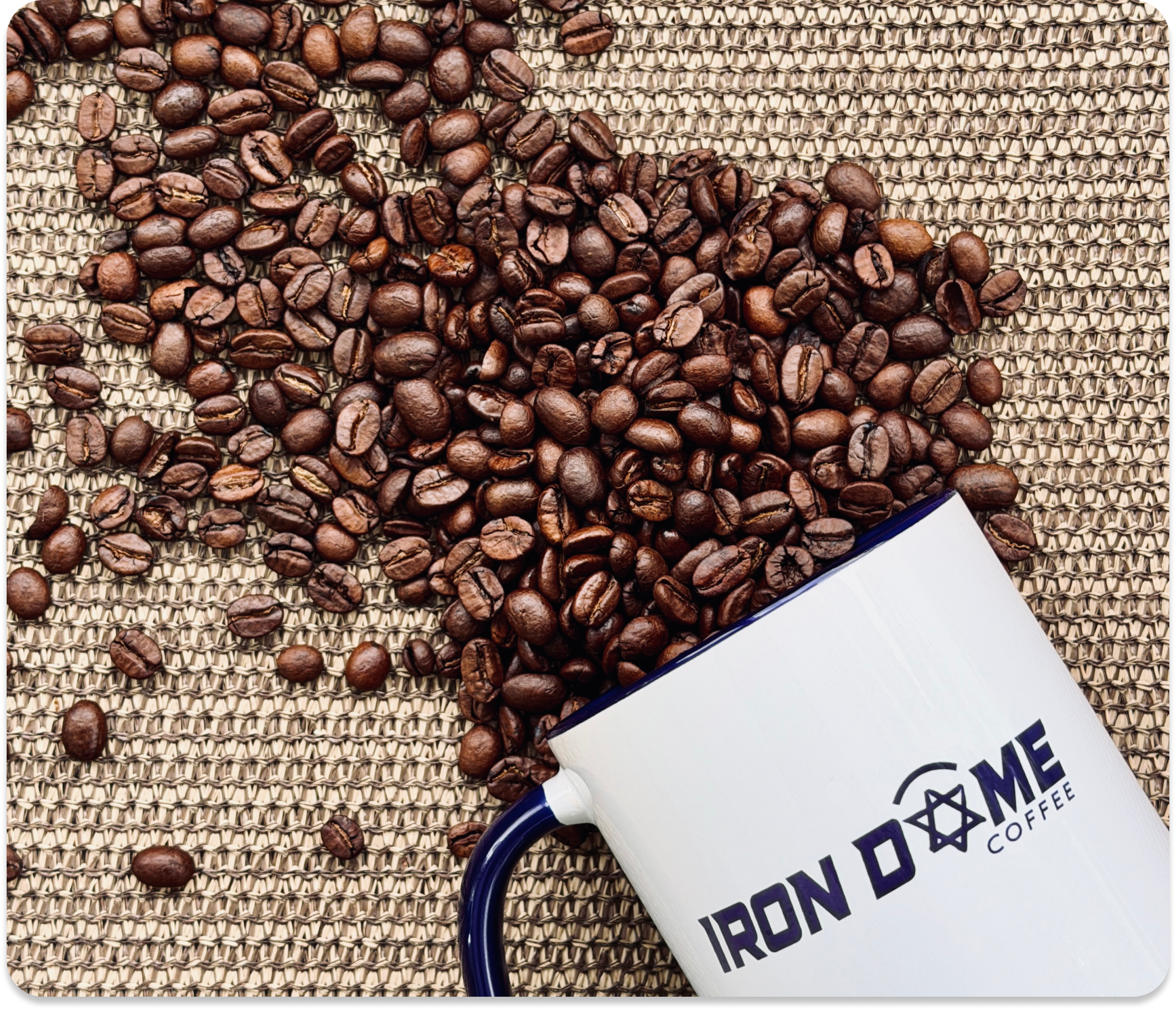 Coffee beans spilling out of a mug labeled 'Iron Dome Coffee' on a textured surface.